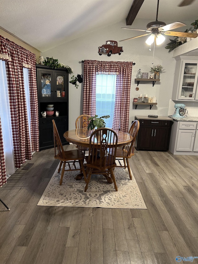 dining area with ceiling fan, wood-type flooring, a textured ceiling, and vaulted ceiling with beams