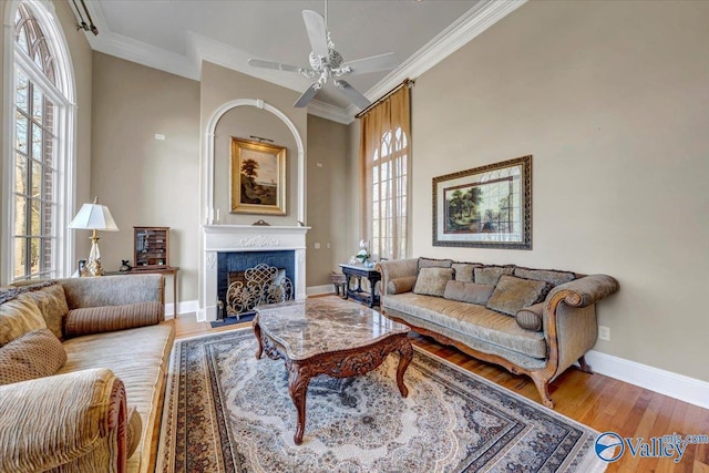 living area with a fireplace, crown molding, baseboards, and wood finished floors