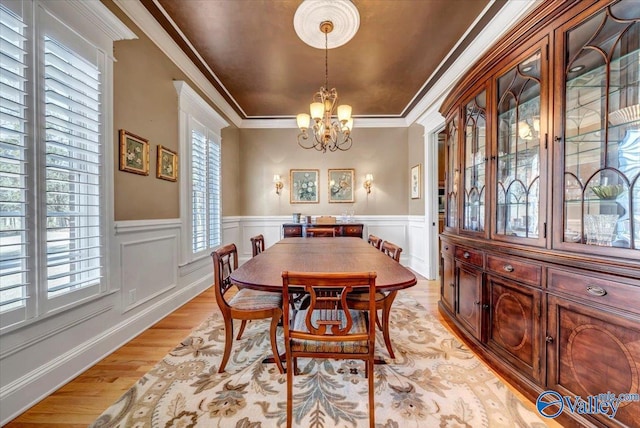 dining area featuring light wood finished floors, ornamental molding, wainscoting, a decorative wall, and a chandelier