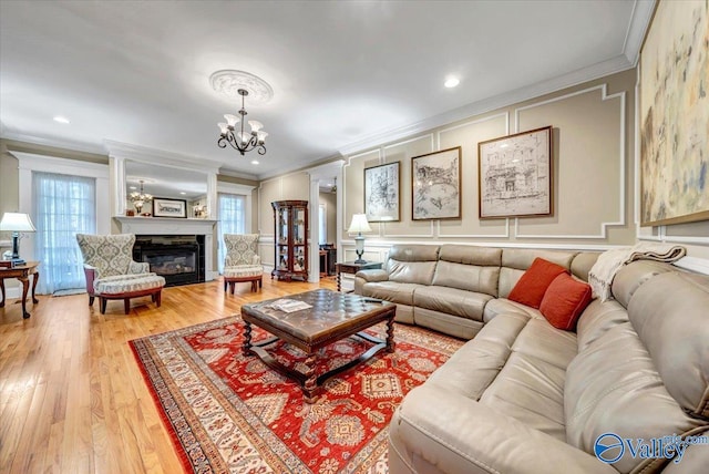 living area with light wood-type flooring, a chandelier, a glass covered fireplace, and ornamental molding