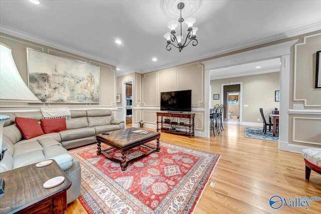 living room featuring ornamental molding, recessed lighting, a decorative wall, light wood finished floors, and a chandelier