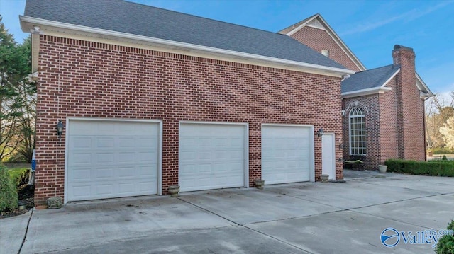 view of side of property with a garage, brick siding, driveway, and a shingled roof