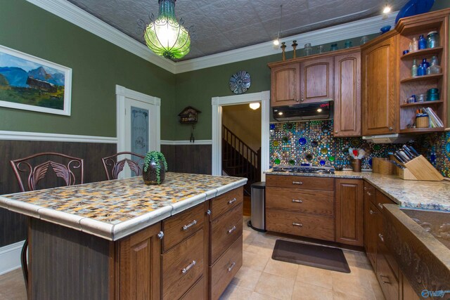 kitchen with a kitchen island, ornamental molding, light tile patterned floors, stainless steel gas stovetop, and tasteful backsplash