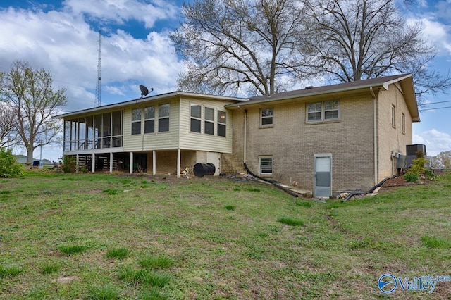 back of property featuring brick siding, a sunroom, and a lawn