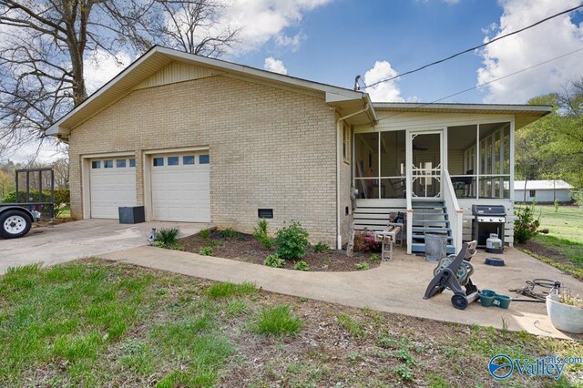 view of side of property with concrete driveway, brick siding, a sunroom, and an attached garage