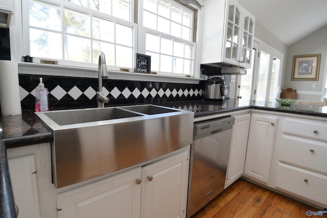 kitchen featuring white cabinetry, vaulted ceiling, light hardwood / wood-style flooring, stainless steel dishwasher, and backsplash
