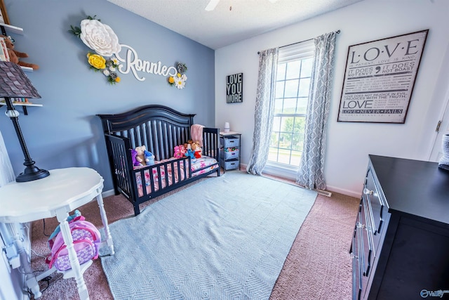 carpeted bedroom featuring a nursery area, baseboards, a ceiling fan, and a textured ceiling