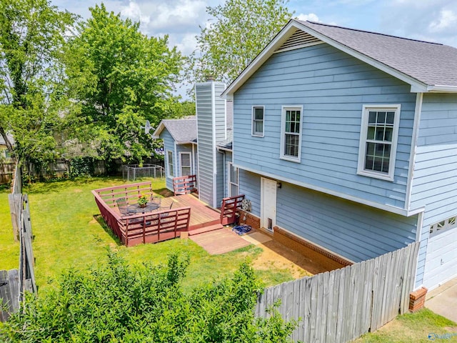 back of property featuring a garage, a wooden deck, a fenced backyard, a shingled roof, and a lawn
