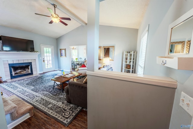 living room featuring a ceiling fan, wood finished floors, a fireplace, baseboards, and lofted ceiling with beams