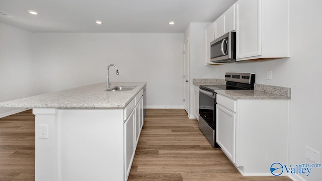 kitchen featuring an island with sink, white cabinetry, sink, light stone counters, and stainless steel appliances