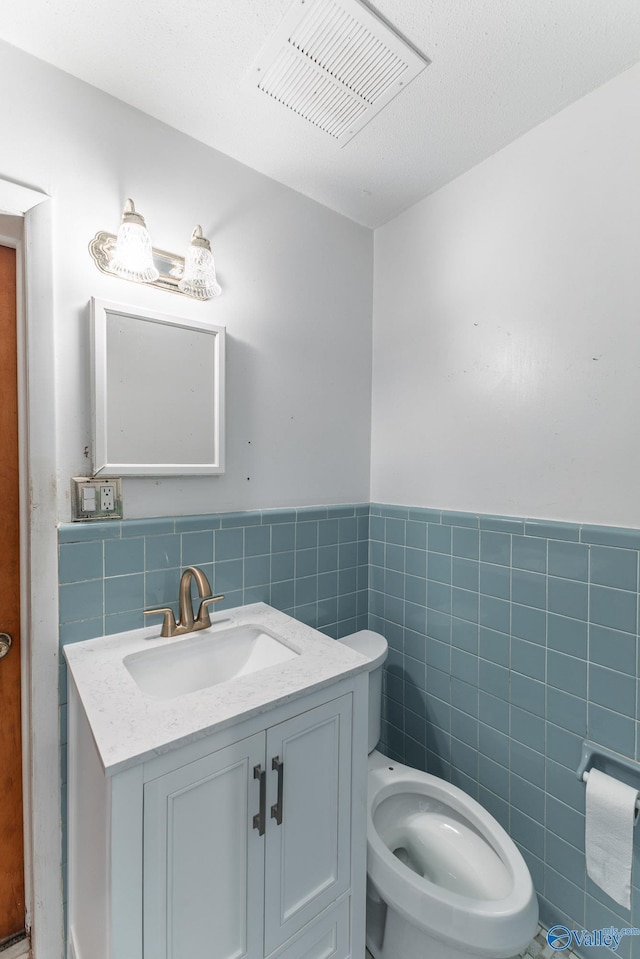 bathroom with toilet, tile walls, wainscoting, visible vents, and vanity