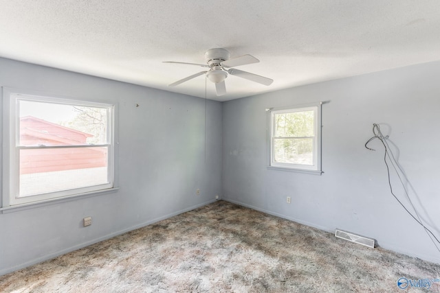 carpeted empty room with a textured ceiling, visible vents, baseboards, and ceiling fan