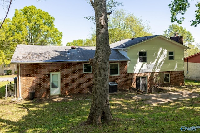 rear view of property with central air condition unit, a chimney, fence, a yard, and brick siding