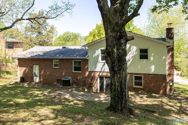 rear view of house featuring brick siding, a yard, central air condition unit, and a chimney