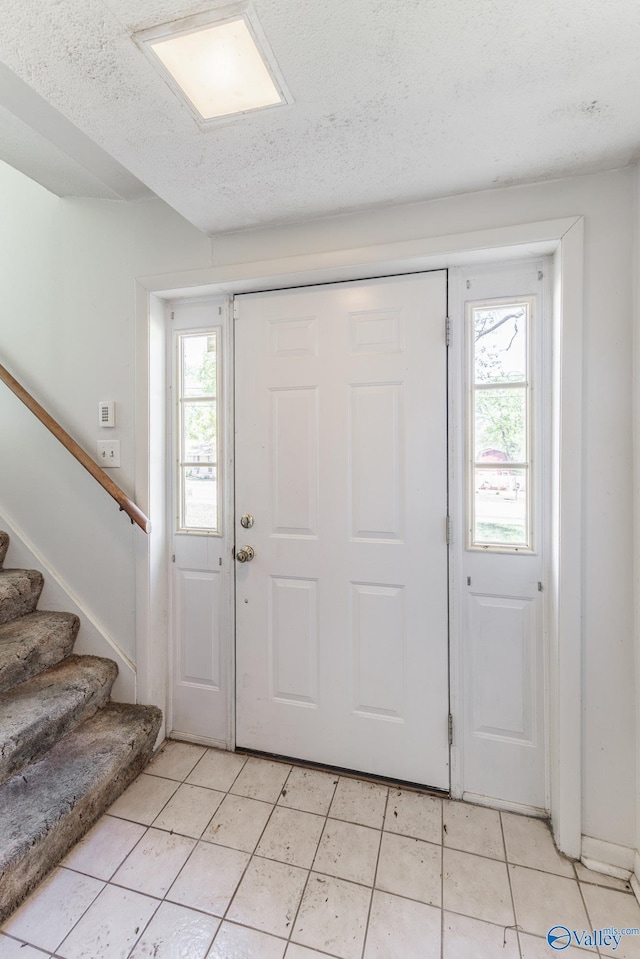 entrance foyer with stairway, light tile patterned flooring, and a textured ceiling