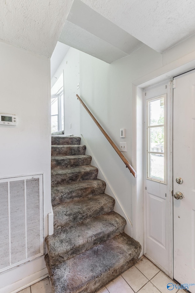 stairs with tile patterned flooring, visible vents, and a textured ceiling