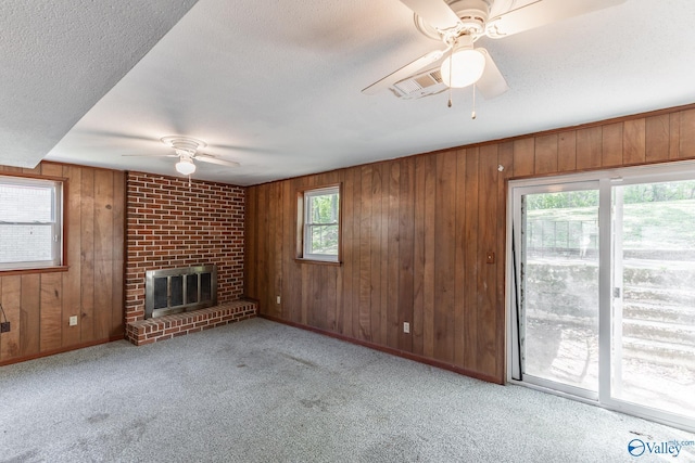 unfurnished living room featuring a textured ceiling, carpet, a ceiling fan, wooden walls, and a fireplace