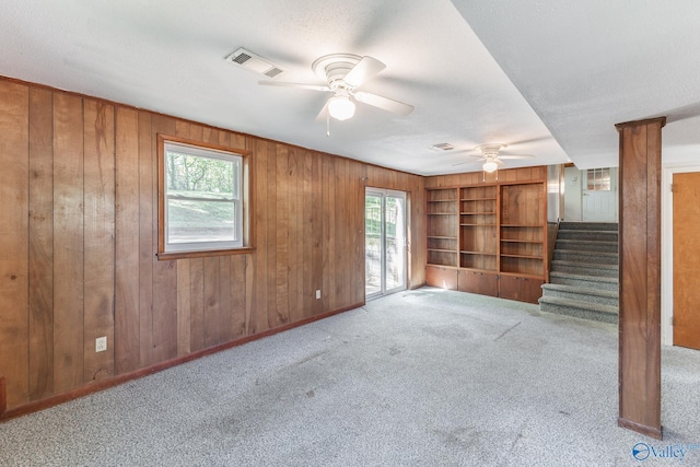 unfurnished living room featuring a healthy amount of sunlight, stairs, ceiling fan, and visible vents