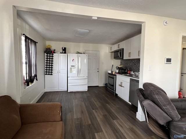 kitchen with dark wood-style flooring, white cabinets, open floor plan, appliances with stainless steel finishes, and tasteful backsplash