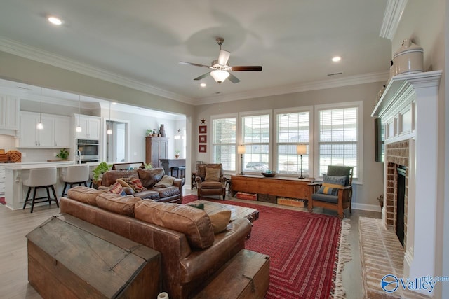 living room featuring ceiling fan, light hardwood / wood-style floors, a brick fireplace, and crown molding