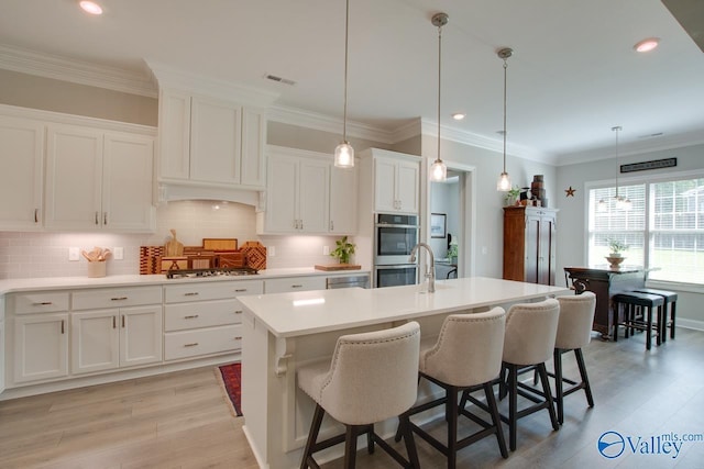 kitchen featuring white cabinets, a center island with sink, light wood-type flooring, and hanging light fixtures