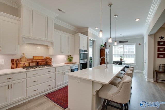 kitchen featuring white cabinetry, light hardwood / wood-style floors, pendant lighting, a kitchen island with sink, and appliances with stainless steel finishes