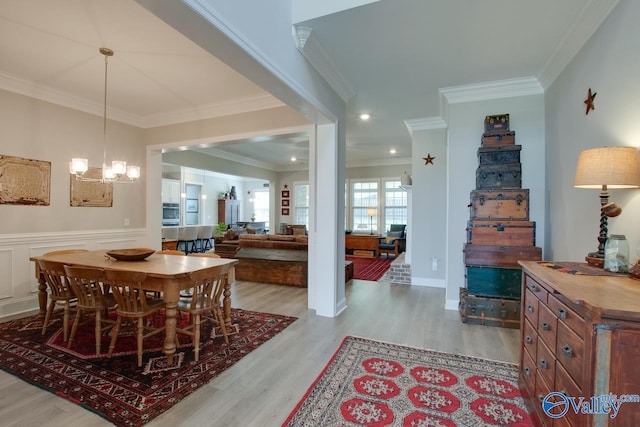 dining space with light wood-type flooring, crown molding, and an inviting chandelier