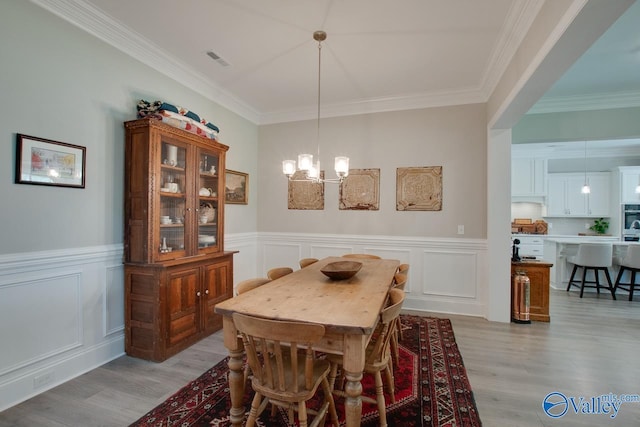 dining area with light hardwood / wood-style floors, ornamental molding, and a chandelier