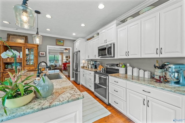 kitchen featuring ornamental molding, a sink, stainless steel appliances, white cabinetry, and light wood-type flooring