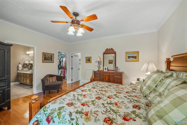 bedroom with a walk in closet, baseboards, ornamental molding, light wood-style flooring, and ensuite bathroom