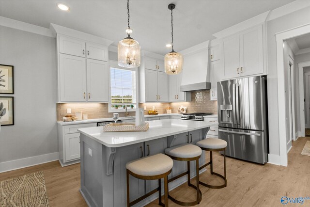 kitchen featuring a kitchen island, premium range hood, stainless steel appliances, light wood-type flooring, and white cabinets