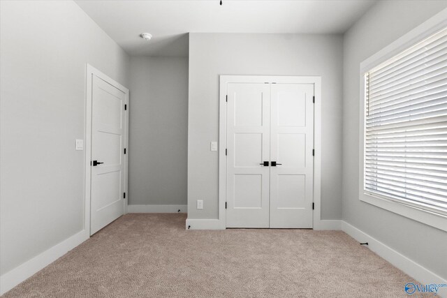 unfurnished bedroom with a closet, multiple windows, and light carpet