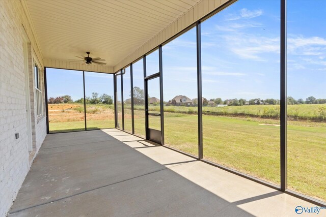 unfurnished sunroom featuring plenty of natural light, ceiling fan, and a rural view