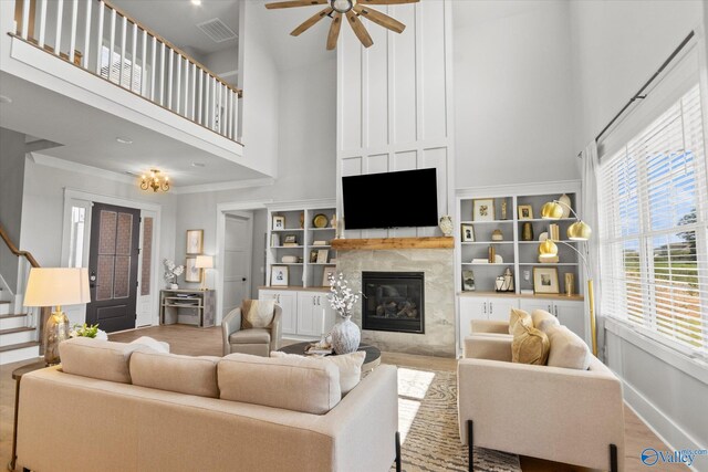 living room featuring a tiled fireplace, crown molding, built in features, ceiling fan, and a towering ceiling