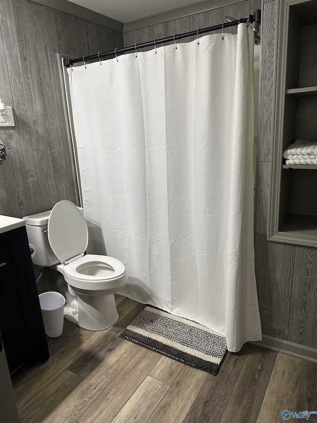 bathroom featuring wood-type flooring, vanity, wooden walls, and toilet