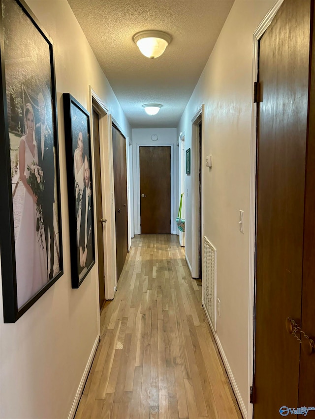 hallway with light hardwood / wood-style floors and a textured ceiling