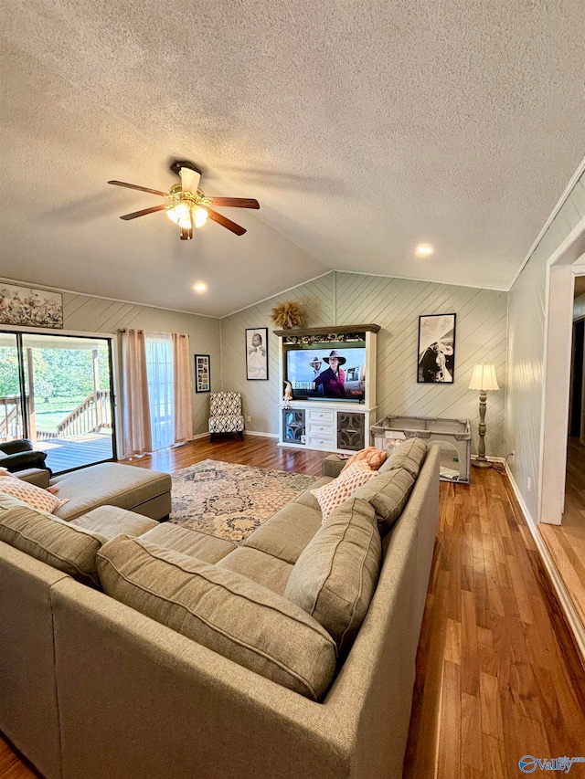 living room featuring ceiling fan, wood-type flooring, vaulted ceiling, wood walls, and a textured ceiling