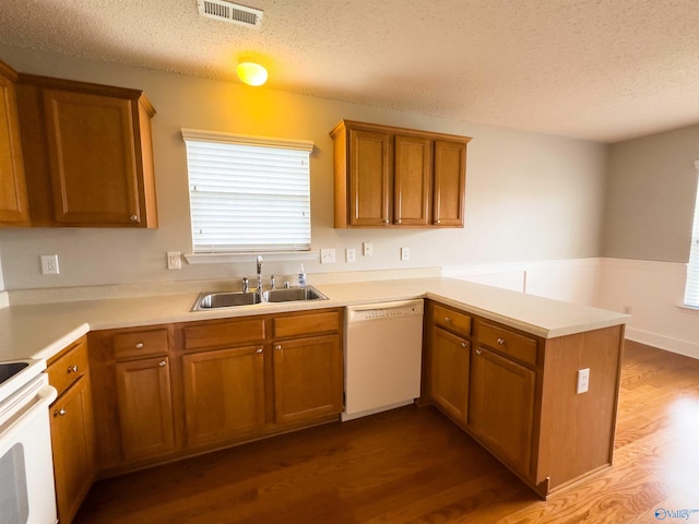 kitchen with a textured ceiling, white appliances, sink, hardwood / wood-style flooring, and kitchen peninsula