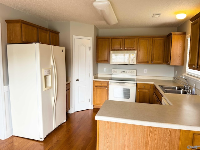 kitchen featuring a textured ceiling, kitchen peninsula, dark wood-type flooring, white appliances, and sink