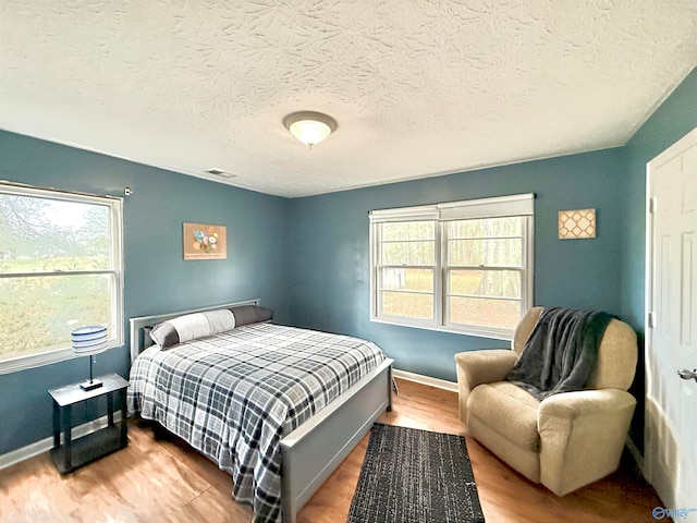 bedroom featuring visible vents, a textured ceiling, baseboards, and wood finished floors