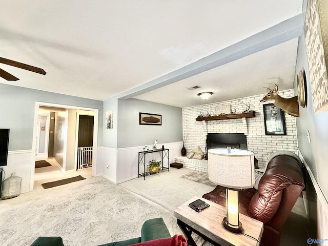 living room with a wainscoted wall, a fireplace, light colored carpet, visible vents, and a ceiling fan