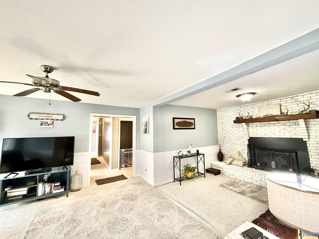 carpeted living area with a wainscoted wall, ceiling fan, a brick fireplace, and visible vents