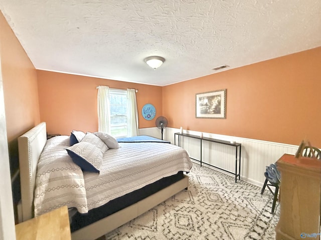 bedroom featuring a wainscoted wall, carpet floors, a textured ceiling, and visible vents