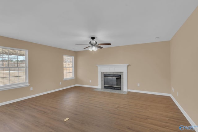 unfurnished living room featuring ceiling fan, a tiled fireplace, and hardwood / wood-style floors