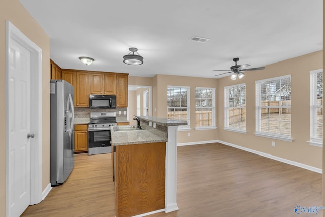 kitchen with stainless steel appliances, tasteful backsplash, light stone countertops, light hardwood / wood-style flooring, and sink