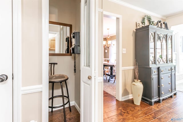 hall featuring crown molding, a chandelier, dark wood finished floors, and baseboards