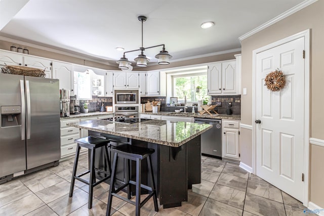 kitchen featuring a kitchen island, white cabinetry, ornamental molding, appliances with stainless steel finishes, and light stone countertops