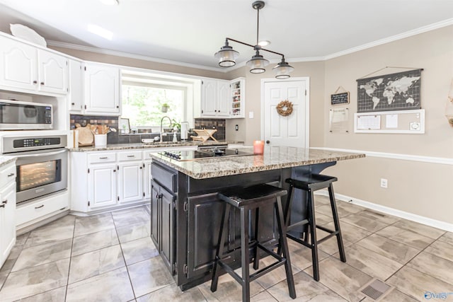 kitchen featuring a center island, appliances with stainless steel finishes, ornamental molding, white cabinets, and light stone countertops