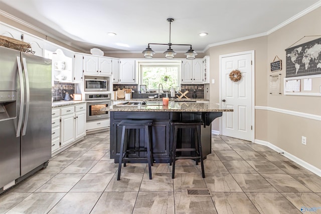 kitchen with light stone counters, appliances with stainless steel finishes, white cabinets, a kitchen island, and a kitchen breakfast bar