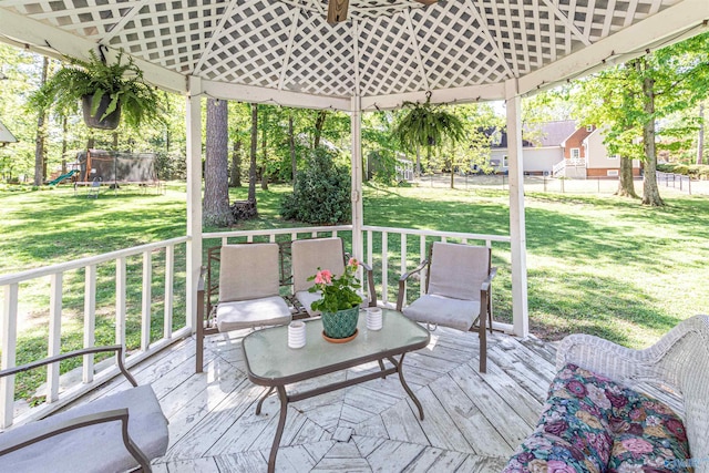 deck featuring a gazebo, a trampoline, fence, and a lawn